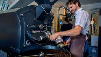 A man roasts coffee beans using a modern roasting machine at a coffee roastery