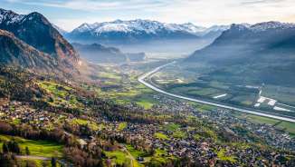 A panoramic view from the hillside overlooking the Rhine Valley, with fields, villages, and snow-capped mountains—a natural idyll in Liechtenstein