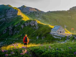 A hiker looks out at the Pfälzerhütte in Liechtenstein, surrounded by green mountain scenery and an Alpine panorama in the evening light
