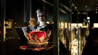 A woman is looking at the Prince's Hat in the Liechtenstein Treasury, surrounded by illuminated display cases.