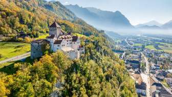 A view of Vaduz Castle with the autumn-colored forest and the town of Vaduz in the valley.