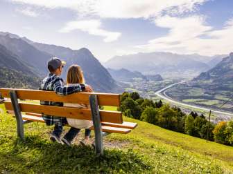 A couple sits on a bench in Triesenberg, looking out over the Rhine Valley in Liechtenstein with its impressive Alpine panorama