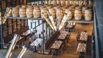 A cozy brewery-style space with long wooden tables, barrel decorations, and stylish lighting