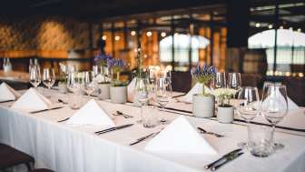 A cozy brewery-style space with long wooden tables, barrel decorations, and stylish lighting