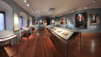 A panoramic view of an exhibition hall at the State Museum featuring historical paintings and display cases.